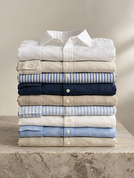 A stack of neatly folded linen shirts in white, sand, navy and sky blue on a marble surface